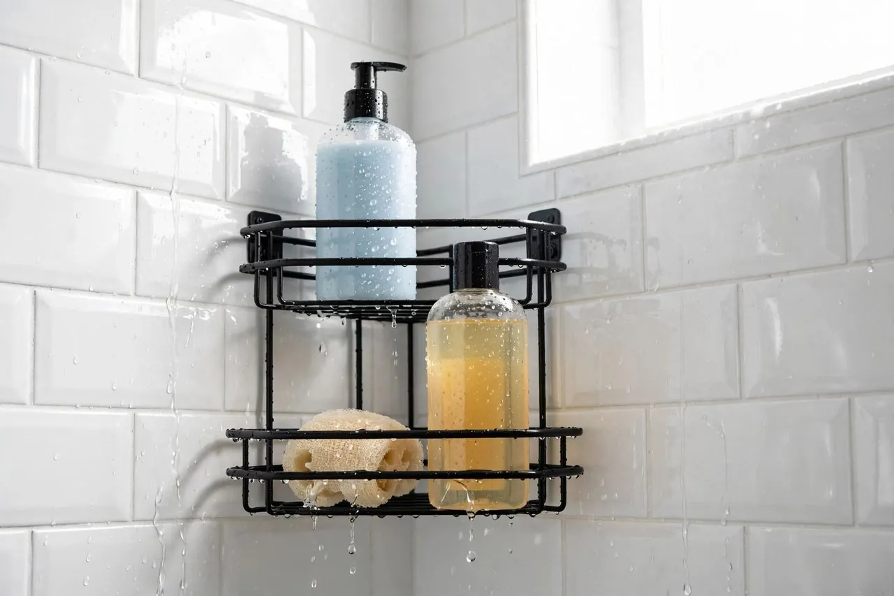Black corner shower caddy mounted on white subway tile, holding shampoo bottles and a sponge