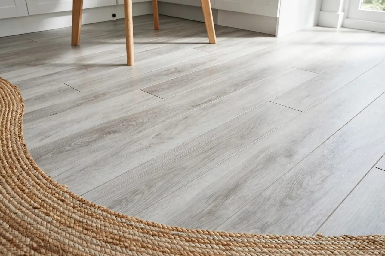 Light grey wood-look peel-and-stick floor planks in a bright rental kitchen, with a woven jute rug at the edge